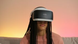 A teenager wearing a VR headset with braided hair sitting indoors, experiencing gaming.